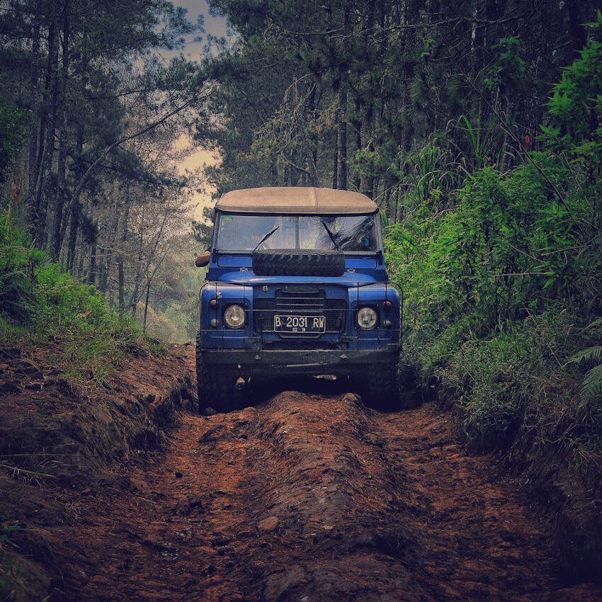 Home Off-road vehicle traversing a rugged dirt path through lush forest in Parongpong, Indonesia.